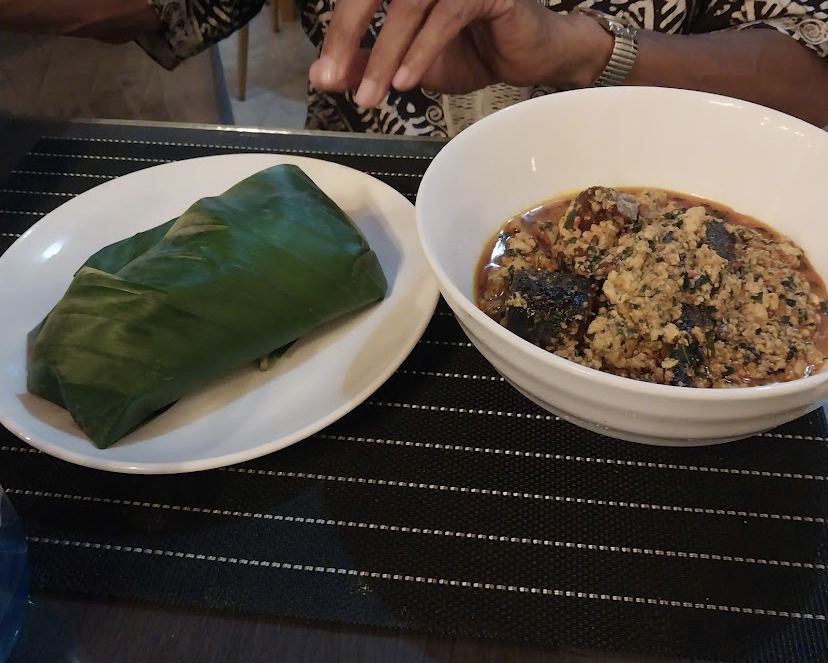 Pounded yam wrapped in leaf with a bowl of egusi